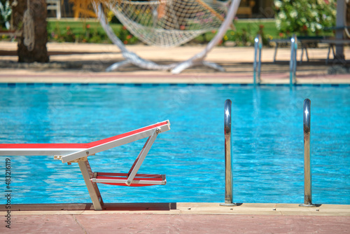 Empty deck chair on swimming pool side in summer resort. Vacations and getaway concept