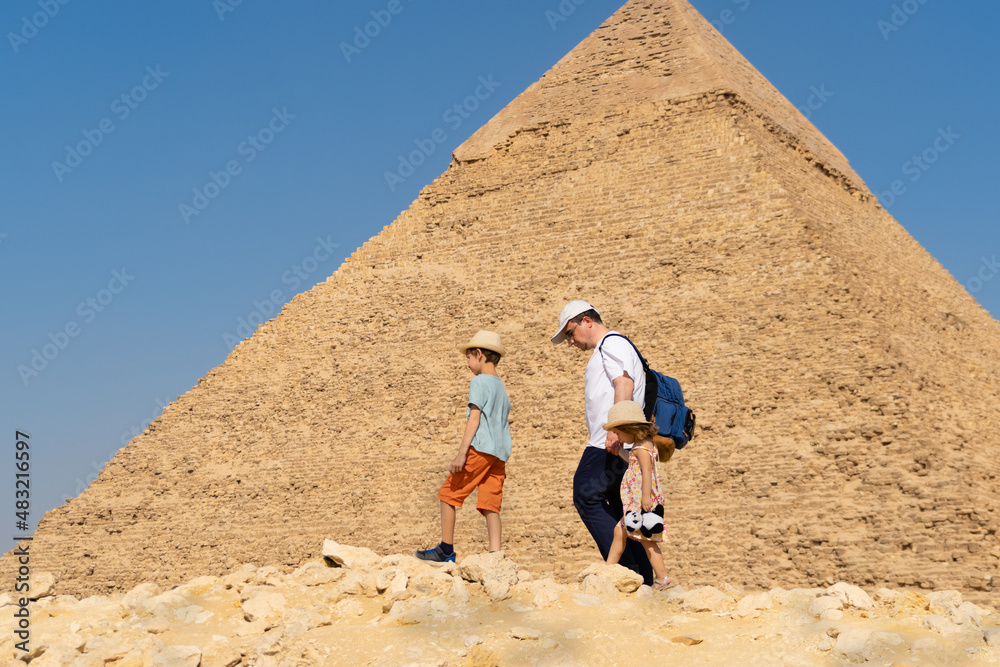 Father and children walk in front of the Chephren pyramid on the Giza plateau - obrazy, fototapety, plakaty 