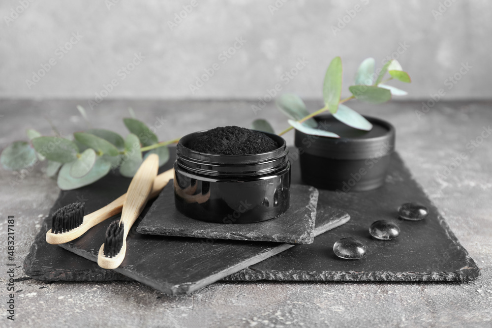 Jar with activated charcoal tooth powder and brushes on grey background Jar with activated charcoal tooth powder and brushes on grey background