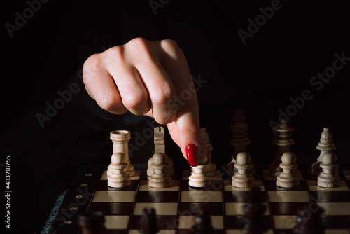 Woman player playing board intelligence game - wooden chess. Female arm with red nails moves piece king, her move. Henpecked, manipulation, psychology, pressure and power concept.