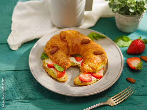 Delicious balanced breakfast - croissant with strawberries, almonds, mint and milk. Turquoise background, decor. Close-up. Restaurant, hotel, cafe, confectionery, home cooking.