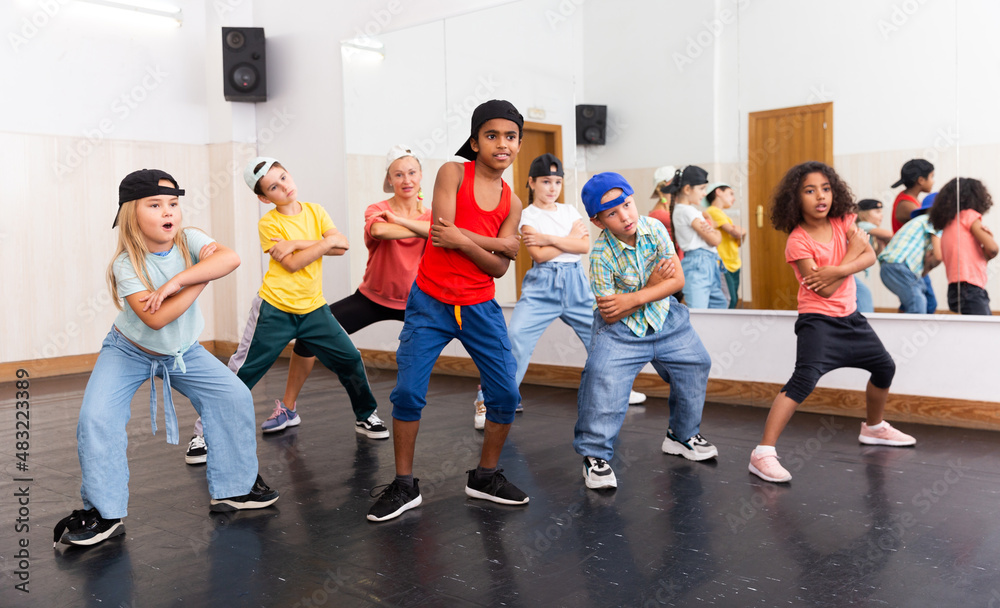 Obraz premium Multiethnic group of children in casual wear training hip hop movements in dance class with female coach..