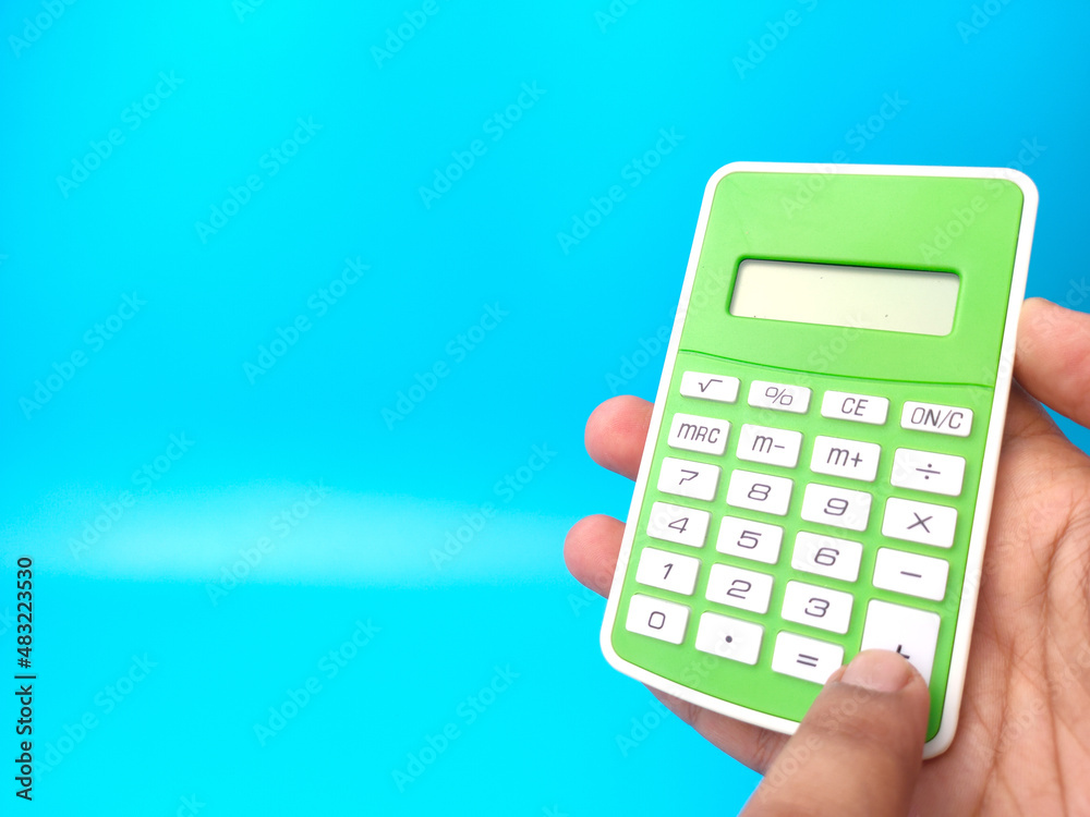 Hand holding green calculator on a blue background with copy space. Hand holding green calculator on a blue background with copy space.