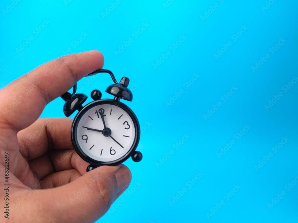 Hand holding black alarm clock on a blue background with copy space. Hand holding black alarm clock on a blue background with copy space.