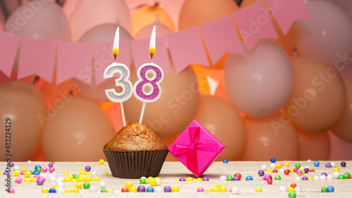 Decorations with balloons and a happy birthday candle with the number 38 for a woman. Happy birthday greetings in pink flowers for thirty-eight years for a girl, copy space. Muffin with a burning cand photo