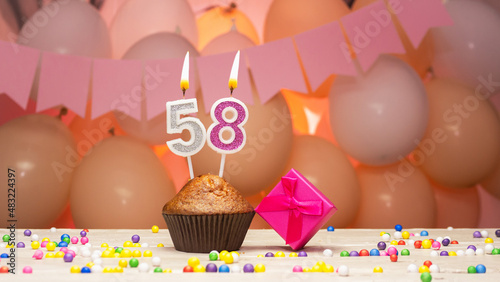  Decorations with balloons and a happy birthday candle with the number 58 for a woman. Happy birthday greetings in pink flowers for fifty-eight years for an adult woman, copy space. Muffin photo