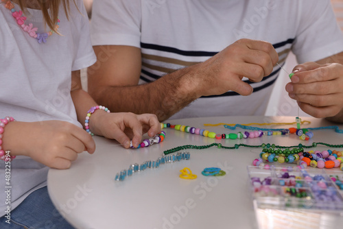 Tableau sur toile Father with his daughter making beaded jewelry at table, closeup