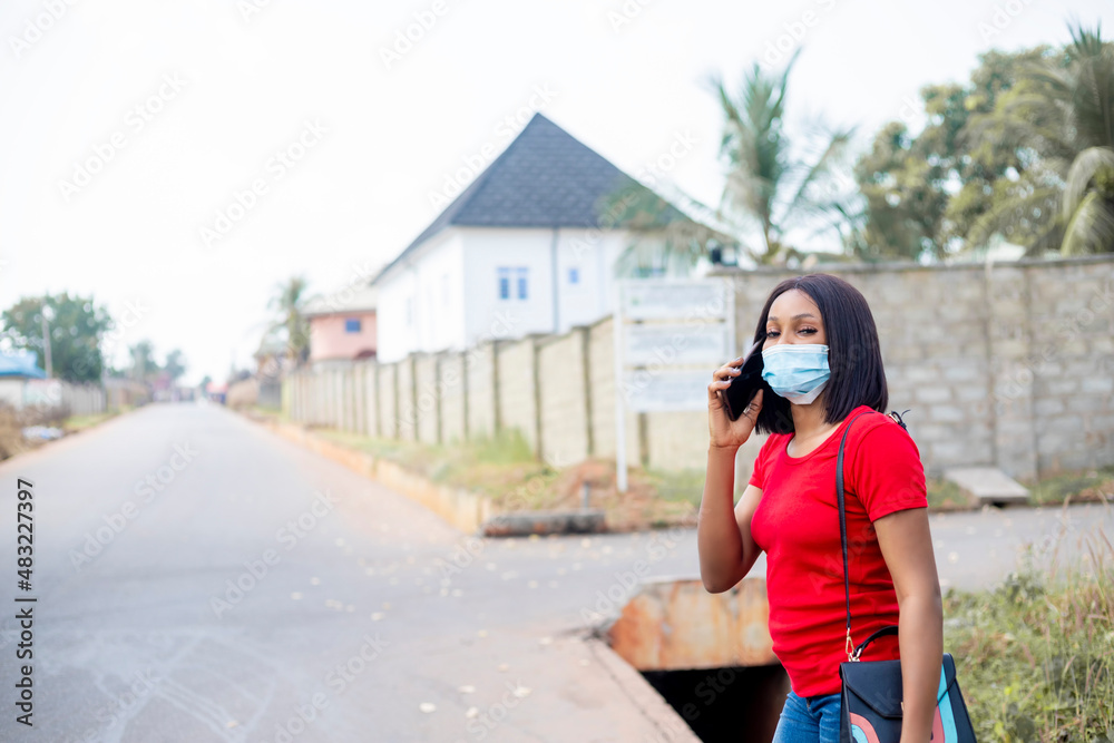 beautiful african college student making a phone call wears face mask standing outside