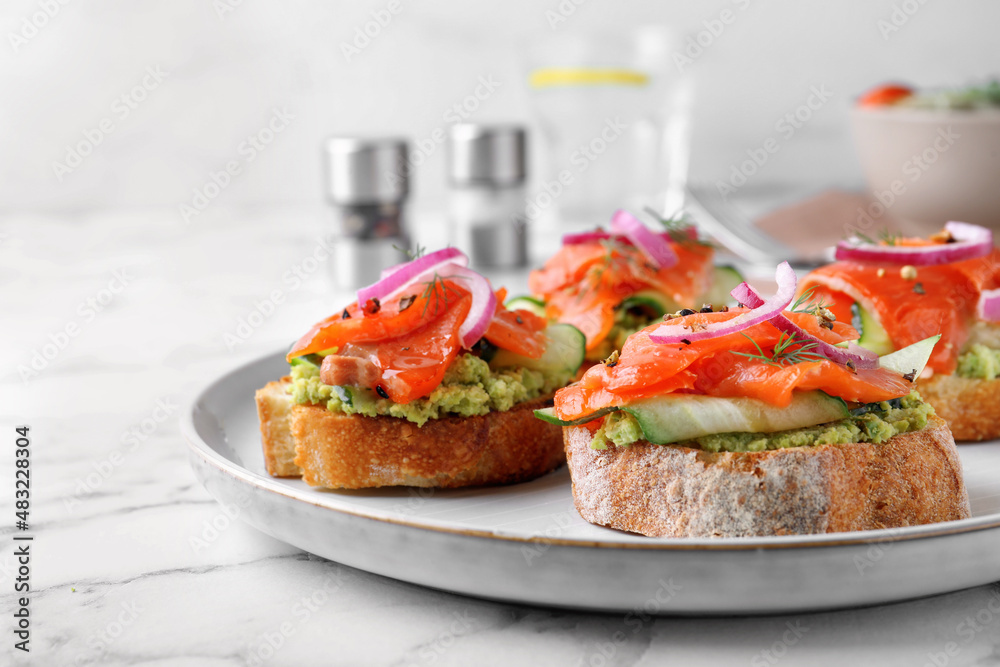 Delicious sandwiches with salmon, avocado, cucumber and onion on white marble table, closeup