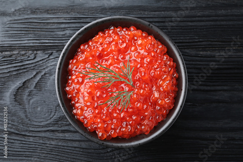 Bowl of delicious red caviar with dill on black wooden table, top view