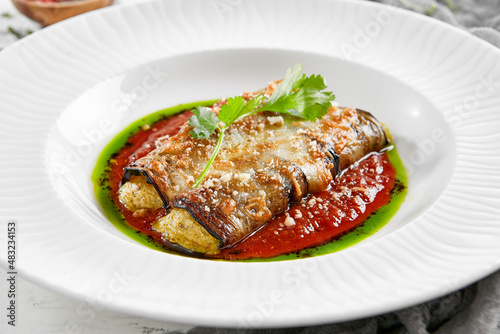 Eggplant rolls stuffed with tomato and cheese. Baked eggplant and cheese rollatini. Eggplant appetizer in white plate on stone background. Plant-based menu.