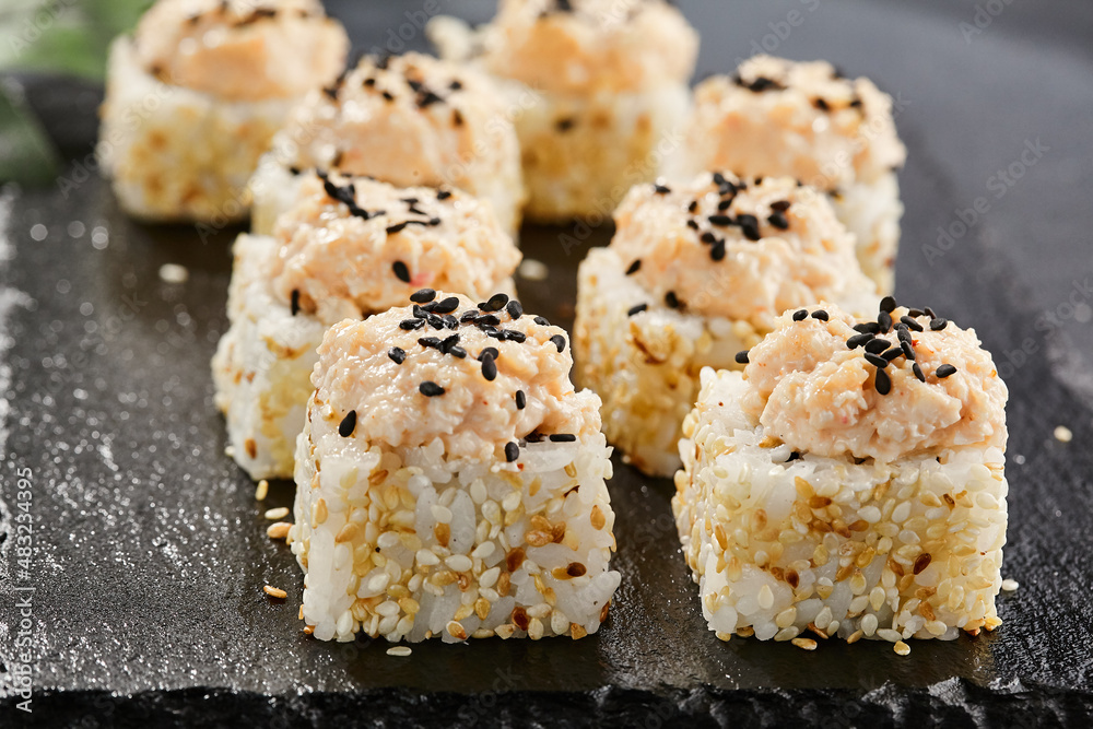 Maki sushi on dark stone table. Sushi roll in seasame and crab topped. Style concept japanesse menu with black background, leaves and hard shadow. Maki sushi on dark stone table. Sushi roll in seasame and crab topped. Style concept japanesse menu with black background, leaves and hard shadow.