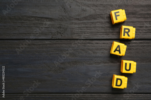 Word Fraud of yellow cubes with letters on black wooden background, flat lay. Space for text photo