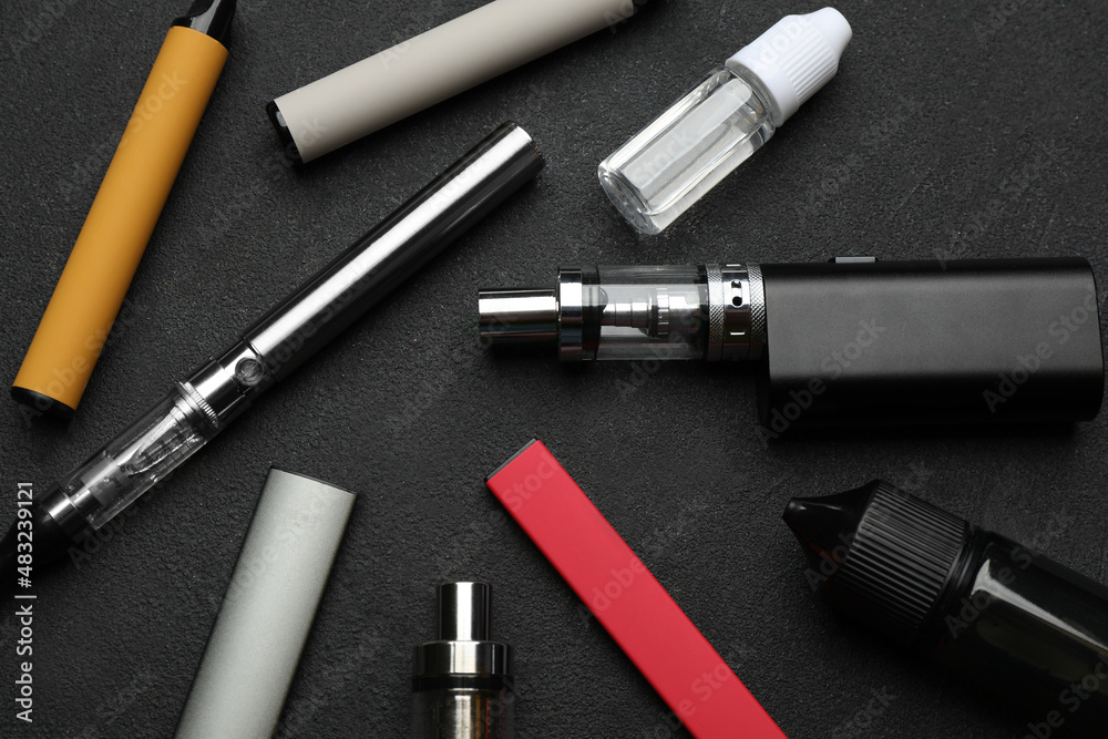 Different electronic cigarettes on black table, flat lay. Smoking alternative Different electronic cigarettes on black table, flat lay. Smoking alternative