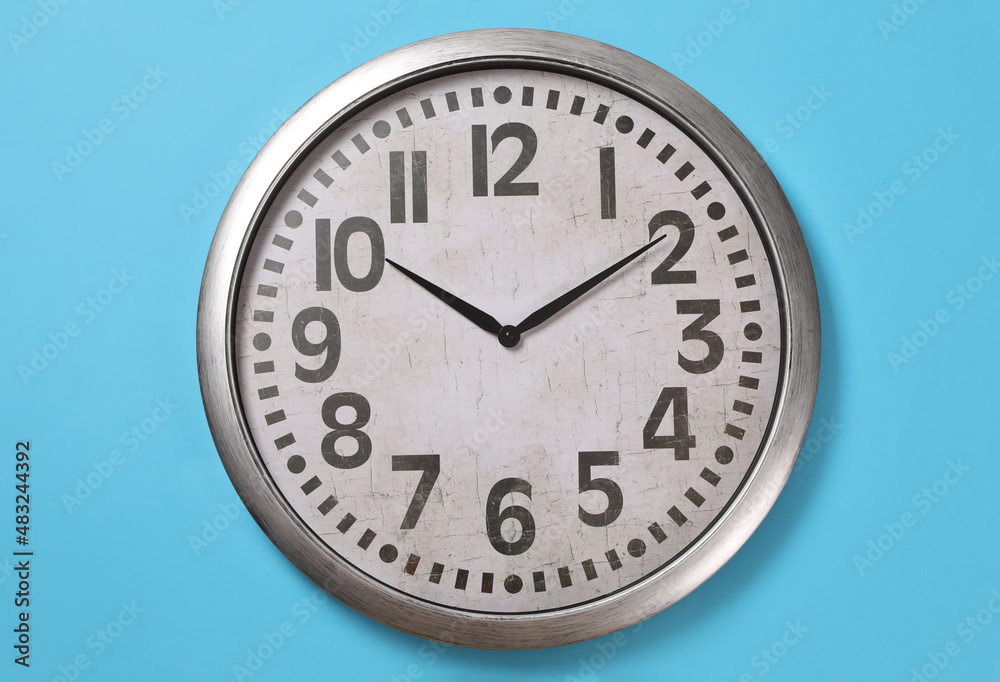 Stylish analog clock hanging on light blue wall Stylish analog clock hanging on light blue wall