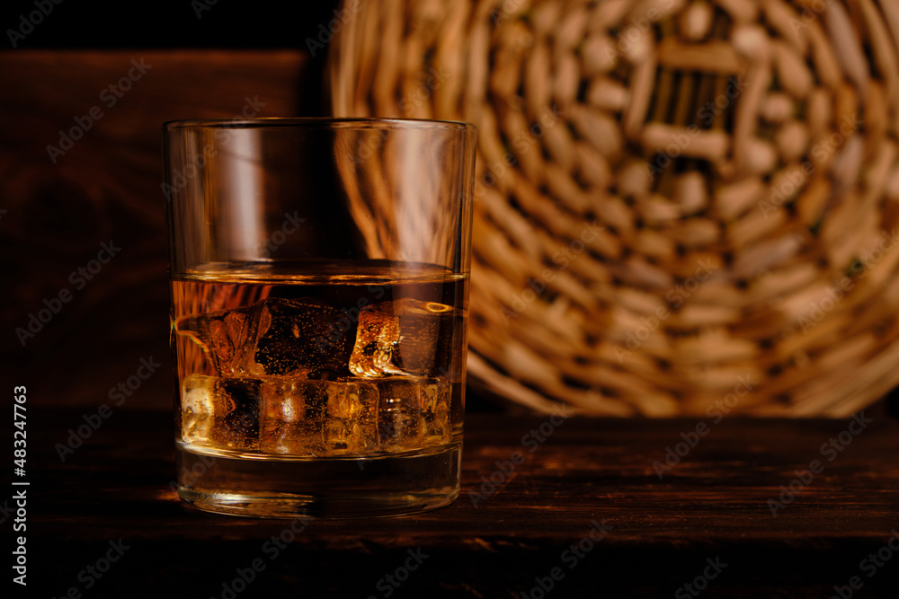 Glass chilled whiskey with ice cubes on wooden background in cellar. Glass chilled whiskey with ice cubes on wooden background in cellar.