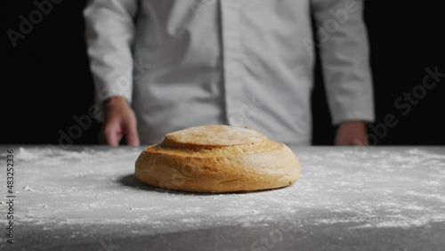 Baker presenting baked bread on table covered with flour photo