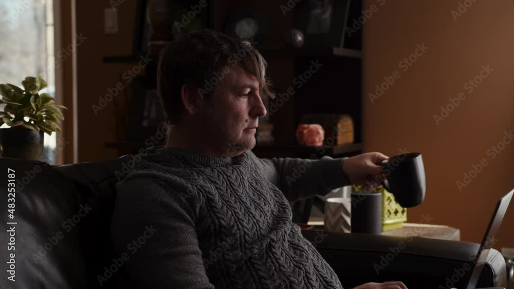 Older Man Working From Home On a Couch and Drinking Coffee During the Day Older Man Working From Home On a Couch and Drinking Coffee During the Day