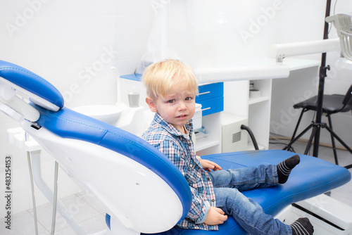 little blond boy is crying in the dentist's chair. primary teeth treatment