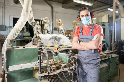 Male carpenter in protective mask standing near wood turning machine