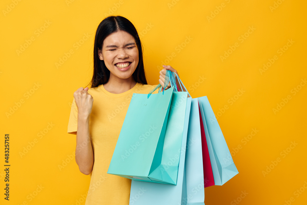 Portrait Asian beautiful young woman in a yellow T-shirt with multicolored shopping bags studio model unaltered Portrait Asian beautiful young woman in a yellow T-shirt with multicolored shopping bags studio model unaltered
