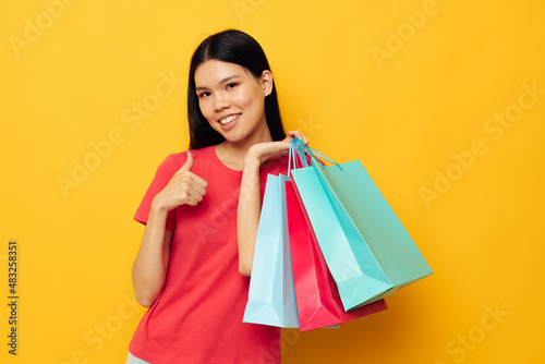 Charming young Asian woman with colorful bags posing shopping fun yellow background unaltered