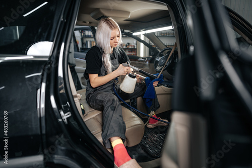 Woman cleaning car salon with polishing spray in car detailing service
