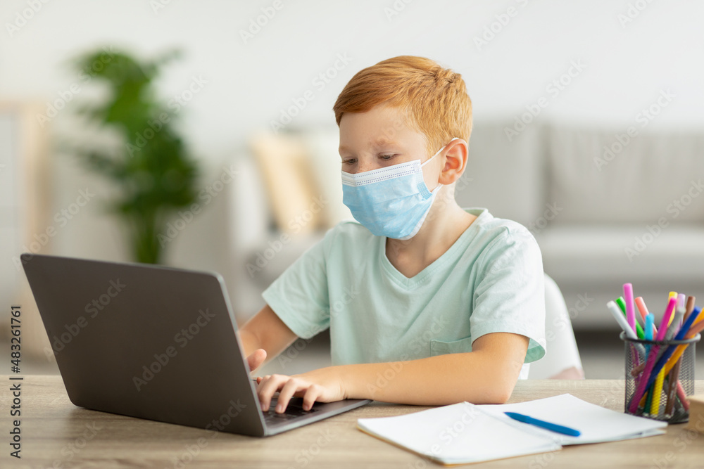 Redhead boy schooler in face mask using laptop, home-schooling concept Redhead boy schooler in face mask using laptop, home-schooling concept