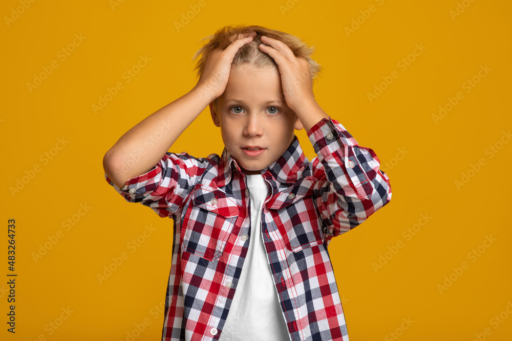 Upset sad surprised caucasian teenage boy presses hands to his head, isolated on yellow background Upset sad surprised caucasian teenage boy presses hands to his head, isolated on yellow background