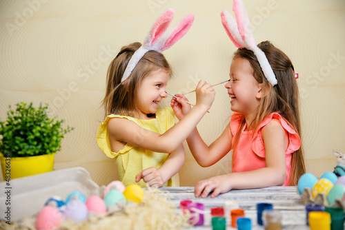 Two little girls in bunnies ears paint Easter eggs and pait each othes. Preparing for Easter 