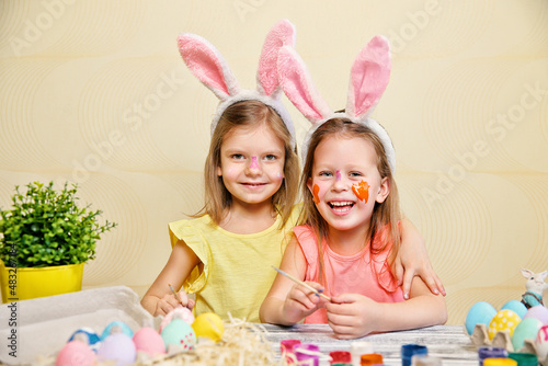 Two cute girls in fun paint and decorate Easter eggs while wear bunny ears. Preparing for Easter