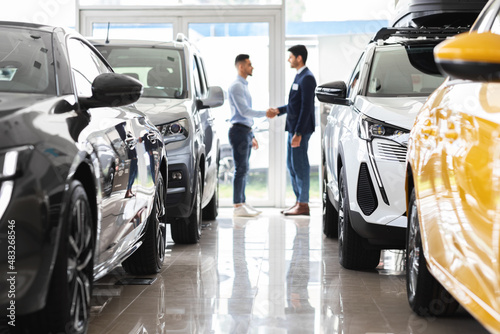 Customer and sales assistant shaking hands, car showroom interior photo