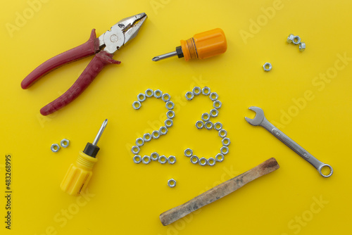 The number 23 of nuts with different tools on a yellow background. Defender of the Fatherland Day