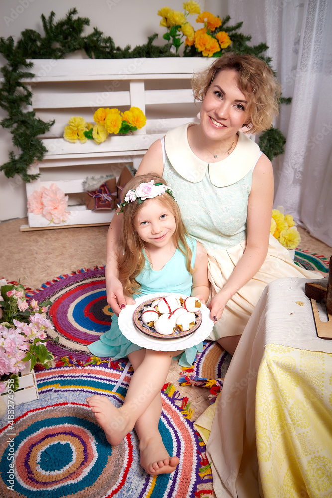 Obraz premium Nice mom and beautiful blonde daughter in room durin spring photo shoot before easter with festive decorated eggs. Happy girl and woman having rest and joy together