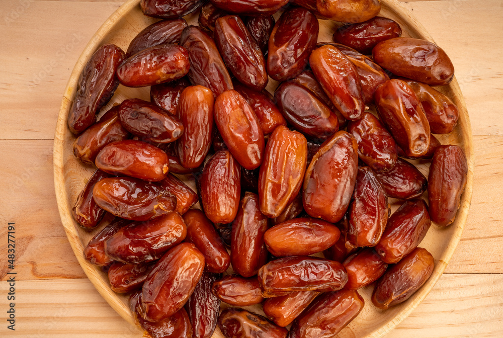 Dried date palm fruit on a wooden plate, date palm fruit with leaf on wooden background Dried date palm fruit on a wooden plate, date palm fruit with leaf on wooden background