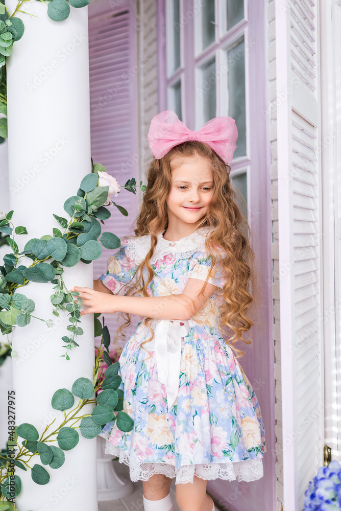 Portrait of a girl who looks like a doll in a delicate light dress and with a bow on her head. Portrait of a girl who looks like a doll in a delicate light dress and with a bow on her head.