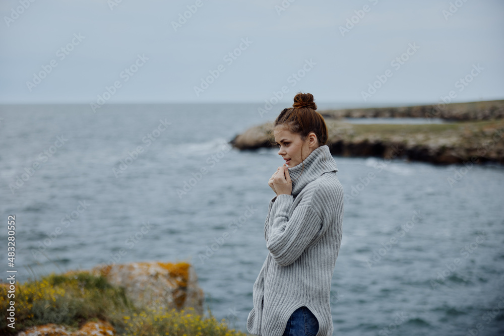 portrait of a woman in a gray sweater stands on a rocky shore nature Lifestyle