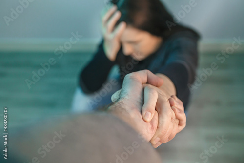 Unrecognizable woman with mental health problems receiving help from man holding her hand. Helping hand concept photo