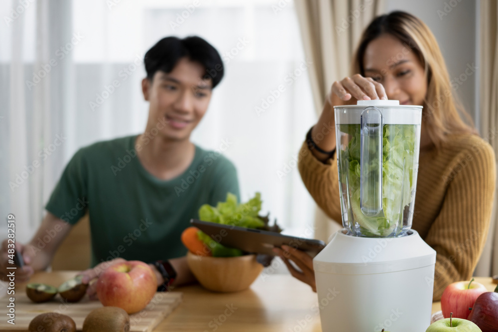 Happy young asian couple making healthy green vegetable smoothie  with organic vegetables in the kitchen.