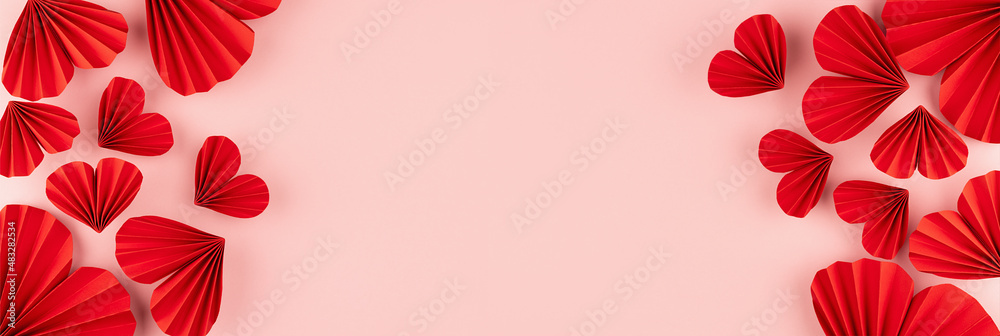 Elegant gentle Valentine day banner with red origami paper hearts fly on soft light pastel pink background, sideways border, frame, copy space, top view.