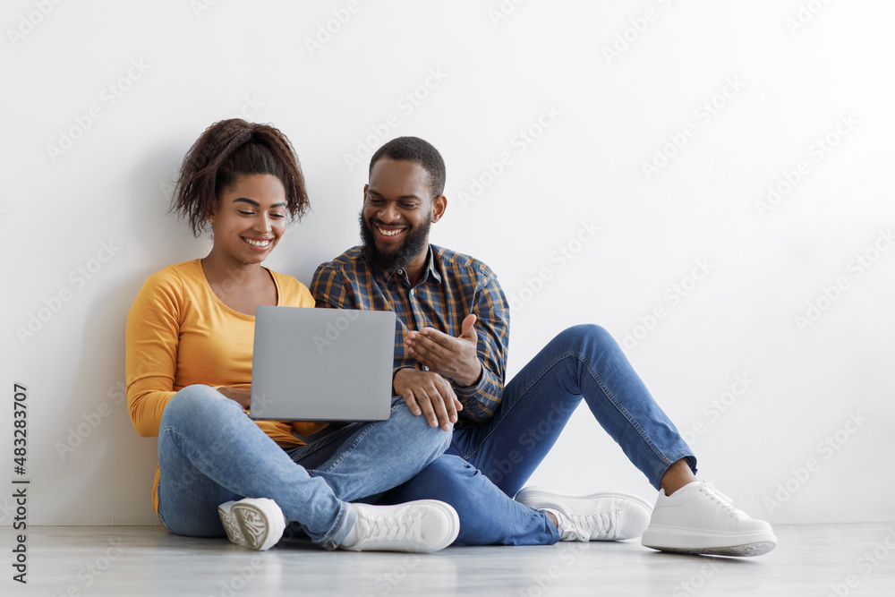 Happy millennial African American husband and wife use laptop to planning new interior design, sits on floor Happy millennial African American husband and wife use laptop to planning new interior design, sits on floor