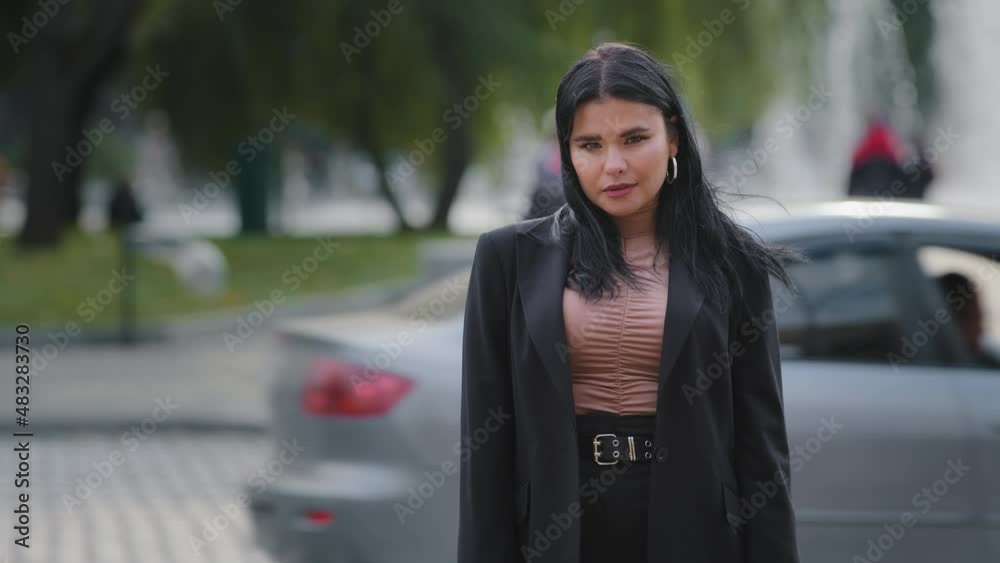 Young confident serious hispanic businesswoman in business suit standing outdoors near roadway pedestrian crossing girl leader employee manager office worker model posing sternly looking at camera Young confident serious hispanic businesswoman in business suit standing outdoors near roadway pedestrian crossing girl leader employee manager office worker model posing sternly looking at camera