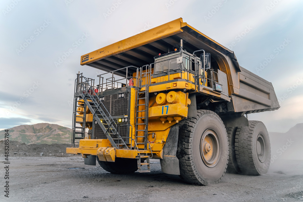 A heavy dump truck drives through an open pit mine.
