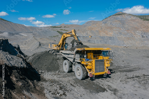 An excavator loads ore into an open-pit dump truck at a gold mine site.