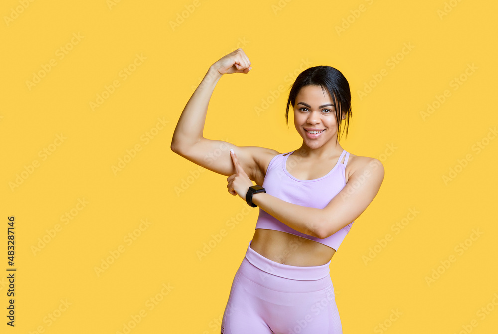 Sports results concept. Excited african american woman showing biceps and pointing on it, yellow background Sports results concept. Excited african american woman showing biceps and pointing on it, yellow background
