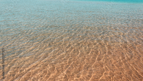 Beautiful yellow-blue gradient sea with waves and light reflection near sandy beach. Summer rest. Water texture