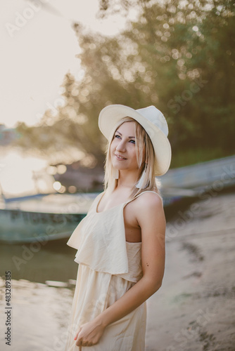 blonde girl in a light dress and a hat near an old boat on the beach © Анна Минина