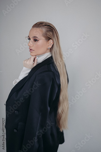 Busy woman, blonde, in a black suit and glasses posing in a room on a gray background