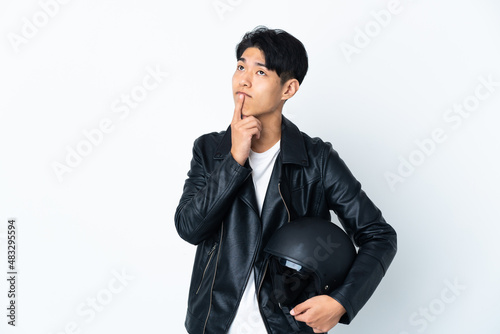 Chinese man with a motorcycle helmet isolated on white background having doubts while looking up