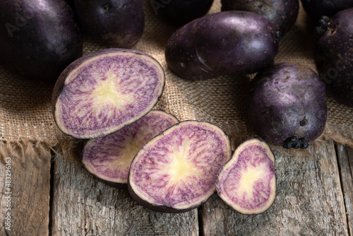 Sliced vitelotte purple potato with whole potatoes on the wooden boards and burlap sackcloth photo